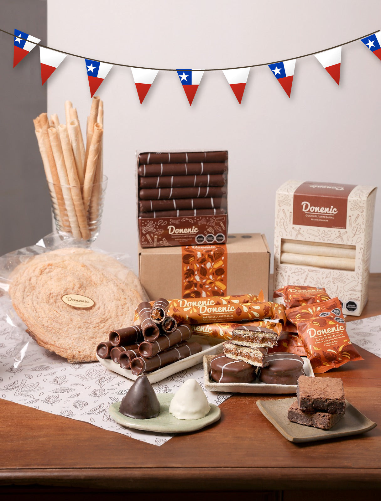 Kit Dieciochero Donenic — surtido de cuchuflíes, barquillos, alfajores, brownies, volcanes y palmeras con guirnalda de banderines chilenos